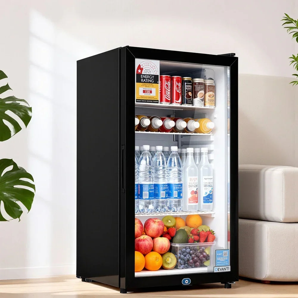 Black glass door mini fridge filled with drinks, bottled water, and assorted fresh fruit in a modern room