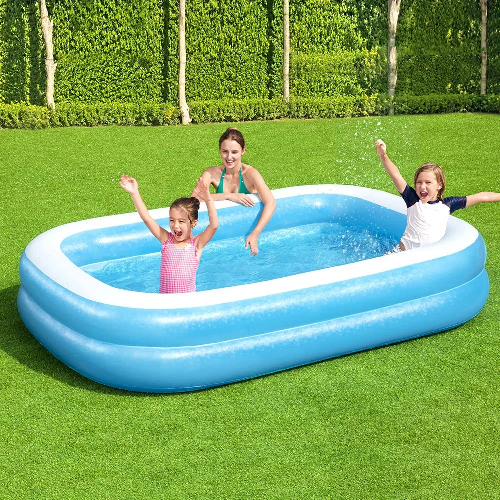 Children playing in a blue inflatable rectangular pool on green grass outdoors