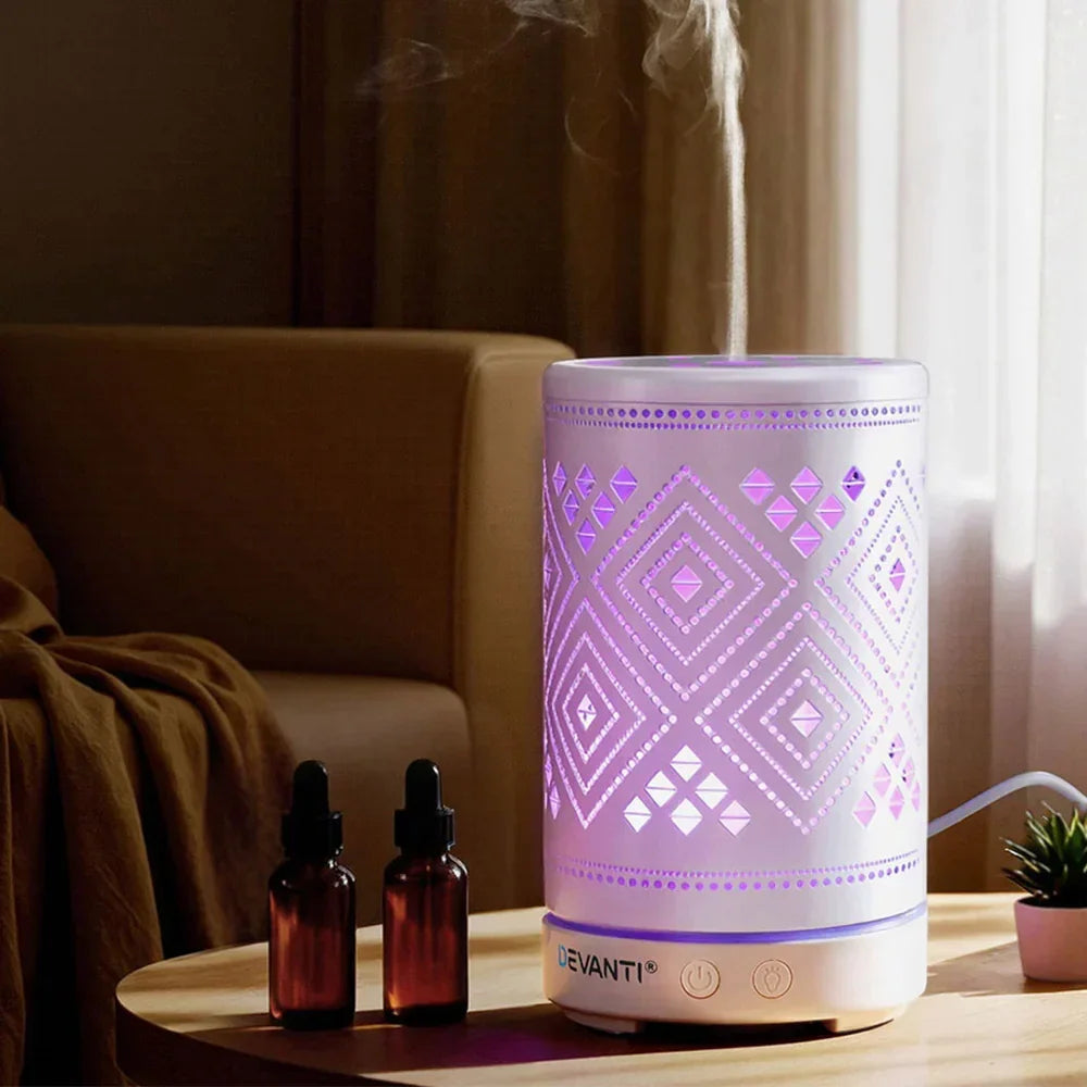 Aromatherapy diffuser with geometric LED lights on a table, steaming, beside essential oil bottles