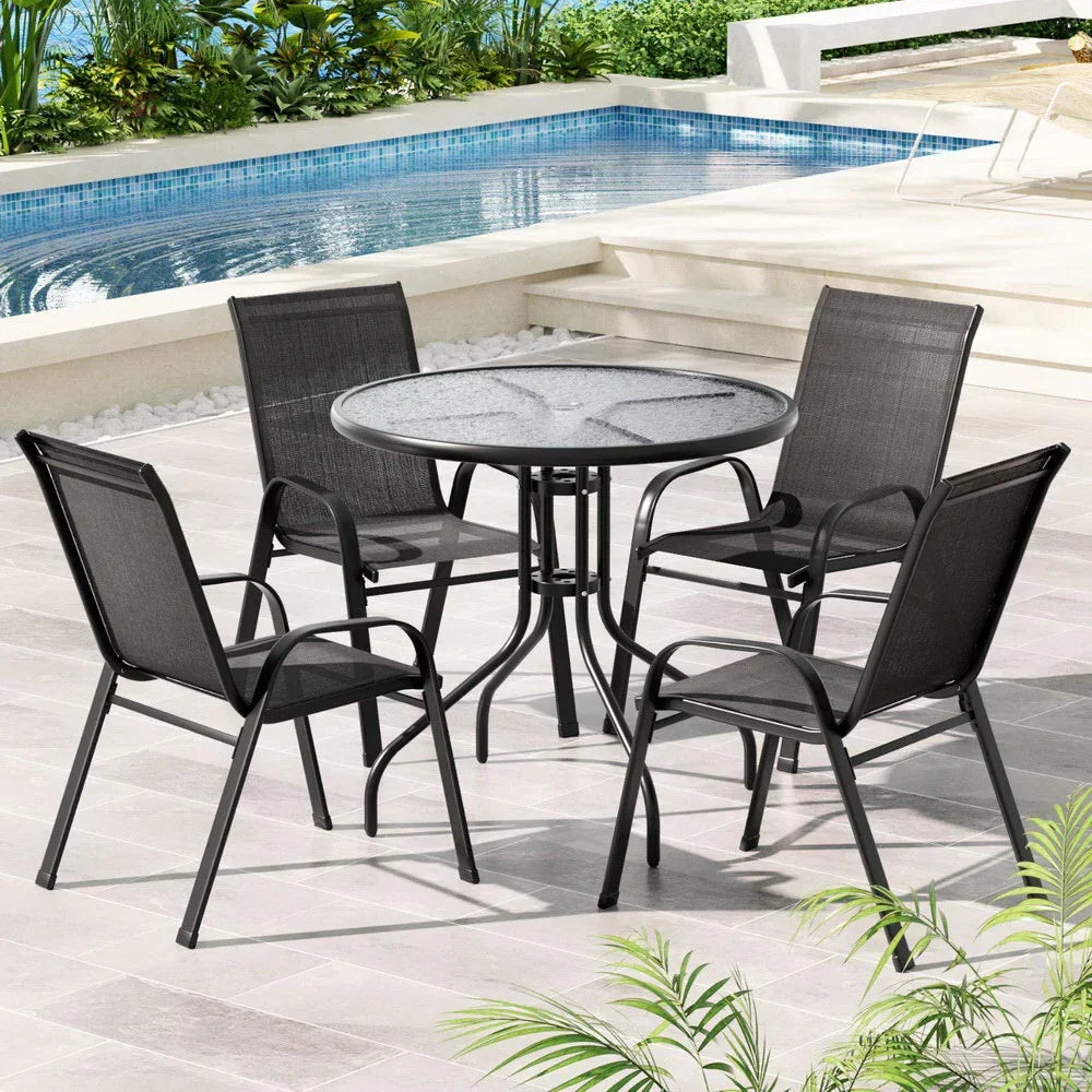 Black outdoor dining set with glass table and four chairs by a pool on tiled patio