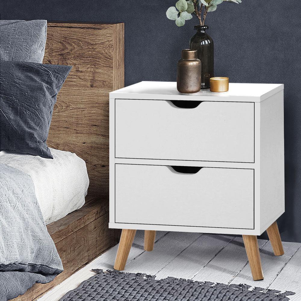 Modern white bedside table with two drawers and wooden legs in a bedroom setting