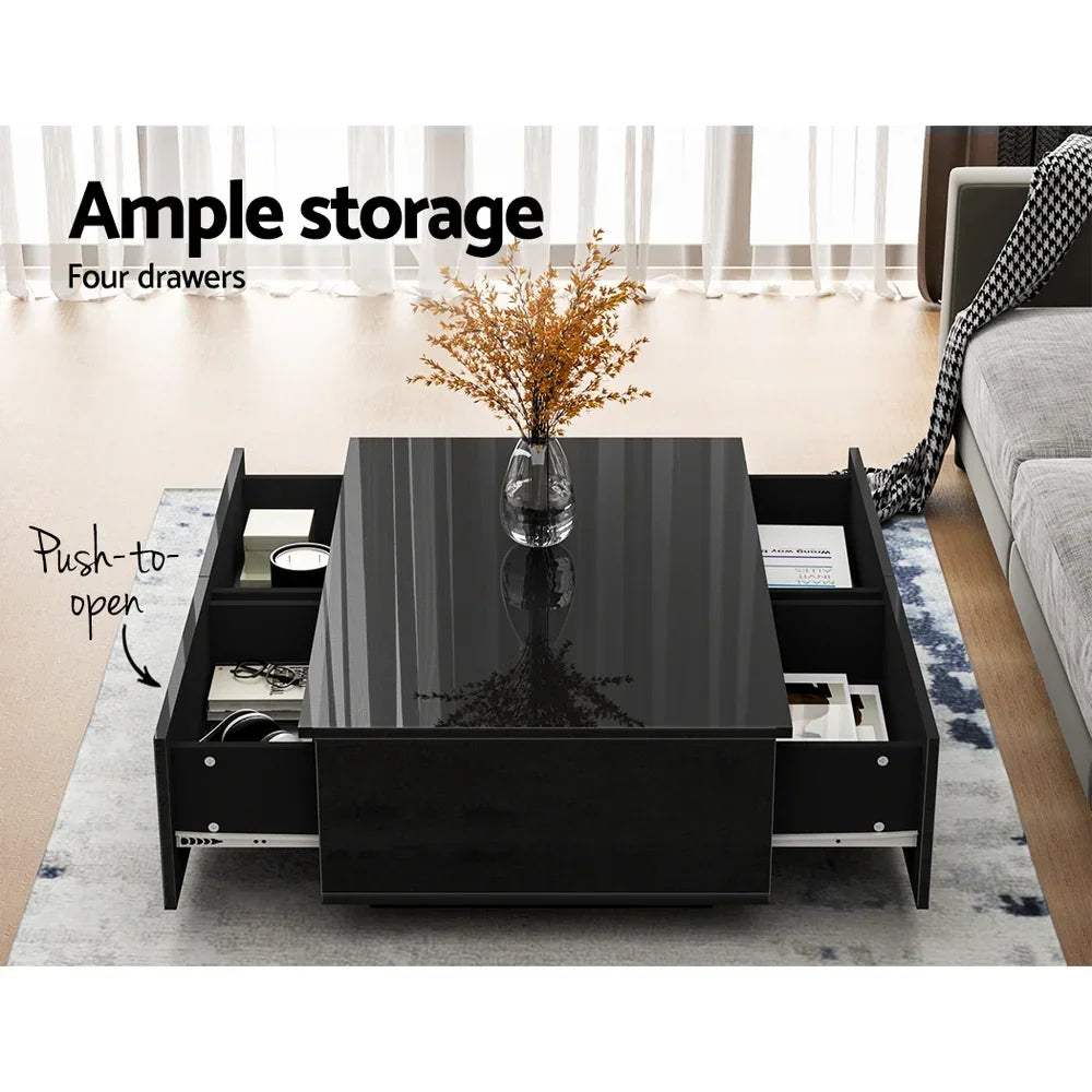 Modern black coffee table with glass top, four push-to-open storage drawers, and vase decor.