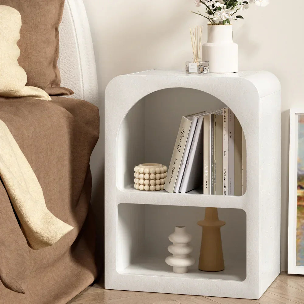Modern white nightstand with open shelves, vases, books, and minimalist decor beside bed