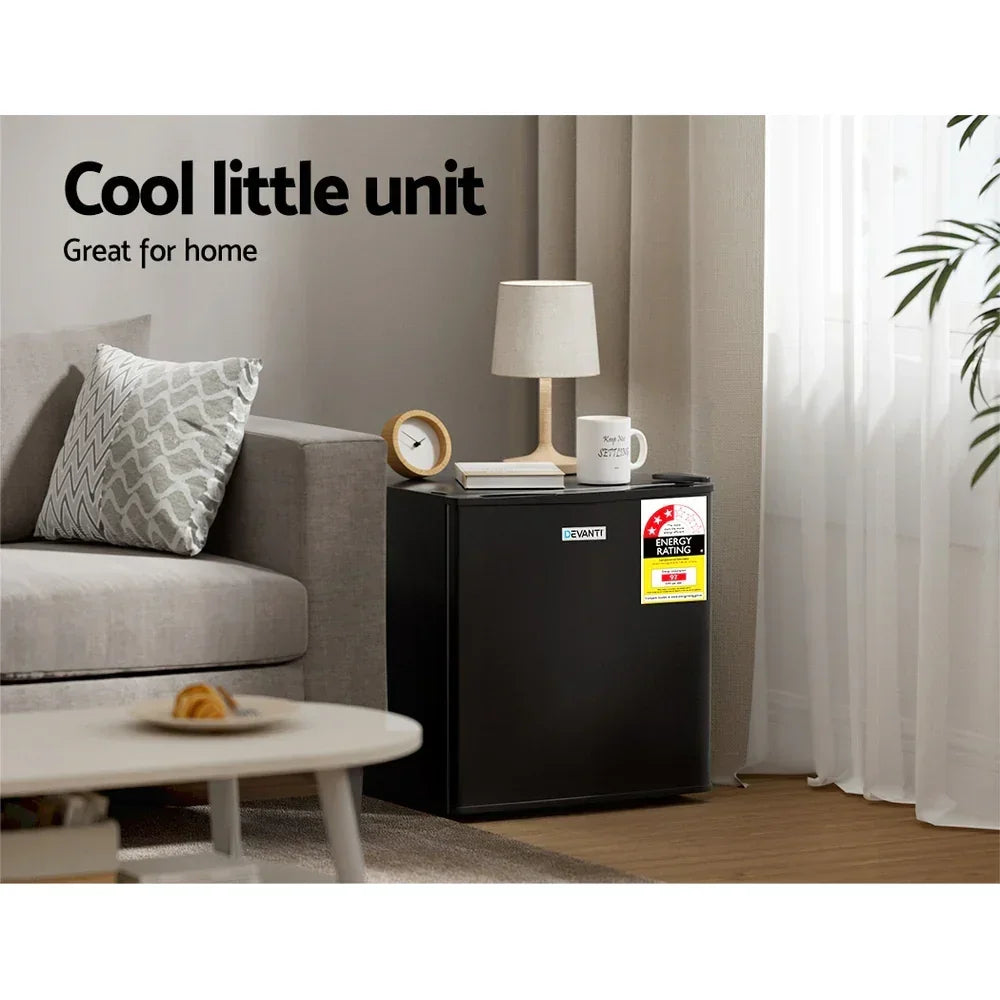 Black mini bar fridge in modern living room beside sofa, energy rating label visible.