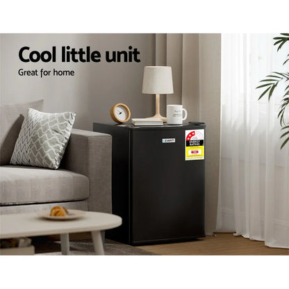 Black mini fridge in modern living room beside sofa, styled with lamp, mug, and clock.