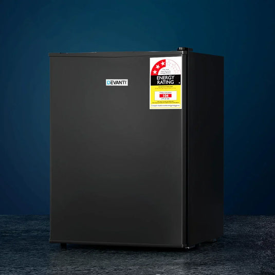 Black compact bar fridge with energy rating label on a dark floor against blue background
