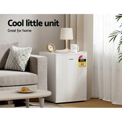 Compact white mini fridge in living room, energy rating label visible, beside sofa and lamp.