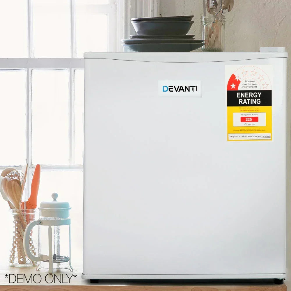 Compact white mini fridge with energy rating sticker in a kitchen setting, utensils beside.