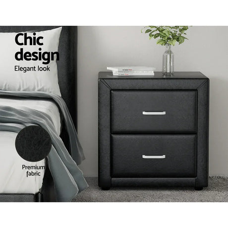 Black two-drawer bedside table with premium fabric, next to a bed and books on top.
