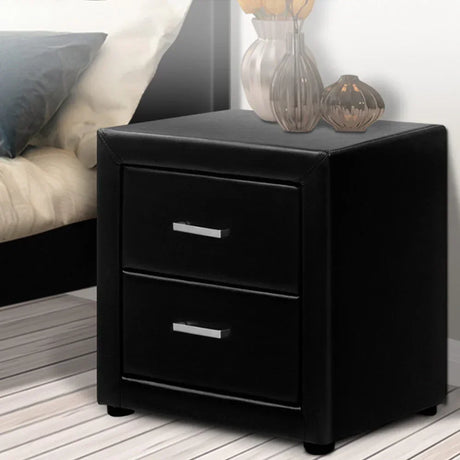 Black two-drawer bedside table with modern silver handles beside a bed on a striped floor