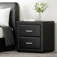 Modern black bedside table with two drawers, metal handles, books, and a glass vase with greenery