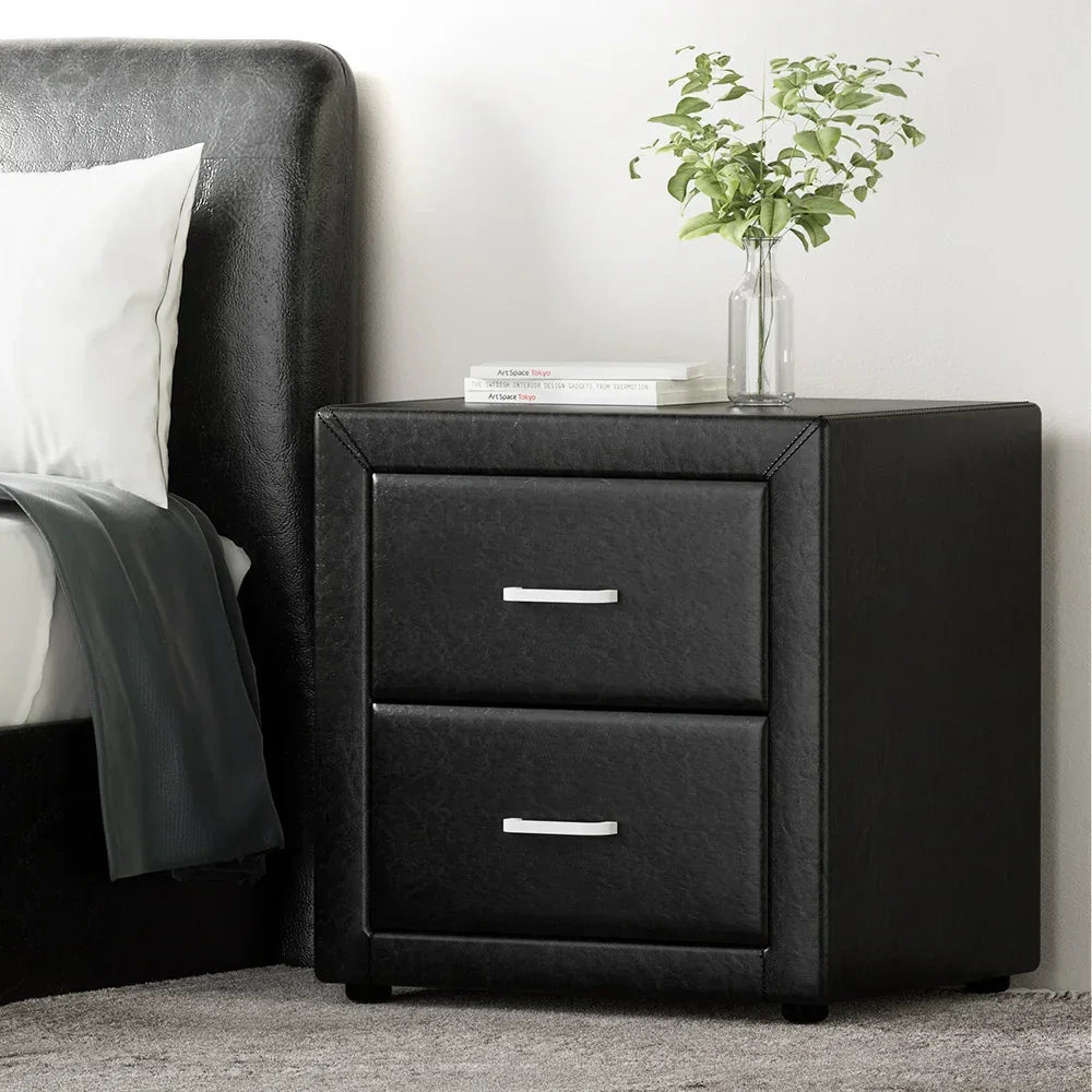Modern black bedside table with two drawers, metal handles, books, and a glass vase with greenery