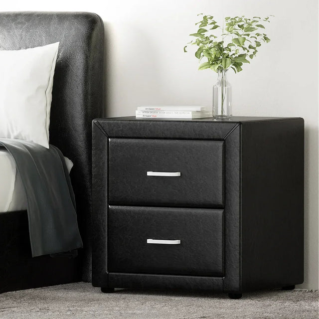 Modern black bedside table with two drawers, metal handles, books, and a glass vase with greenery