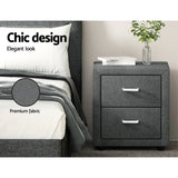 Grey fabric bedside table with two drawers, modern bed, decor books and vase with plant.