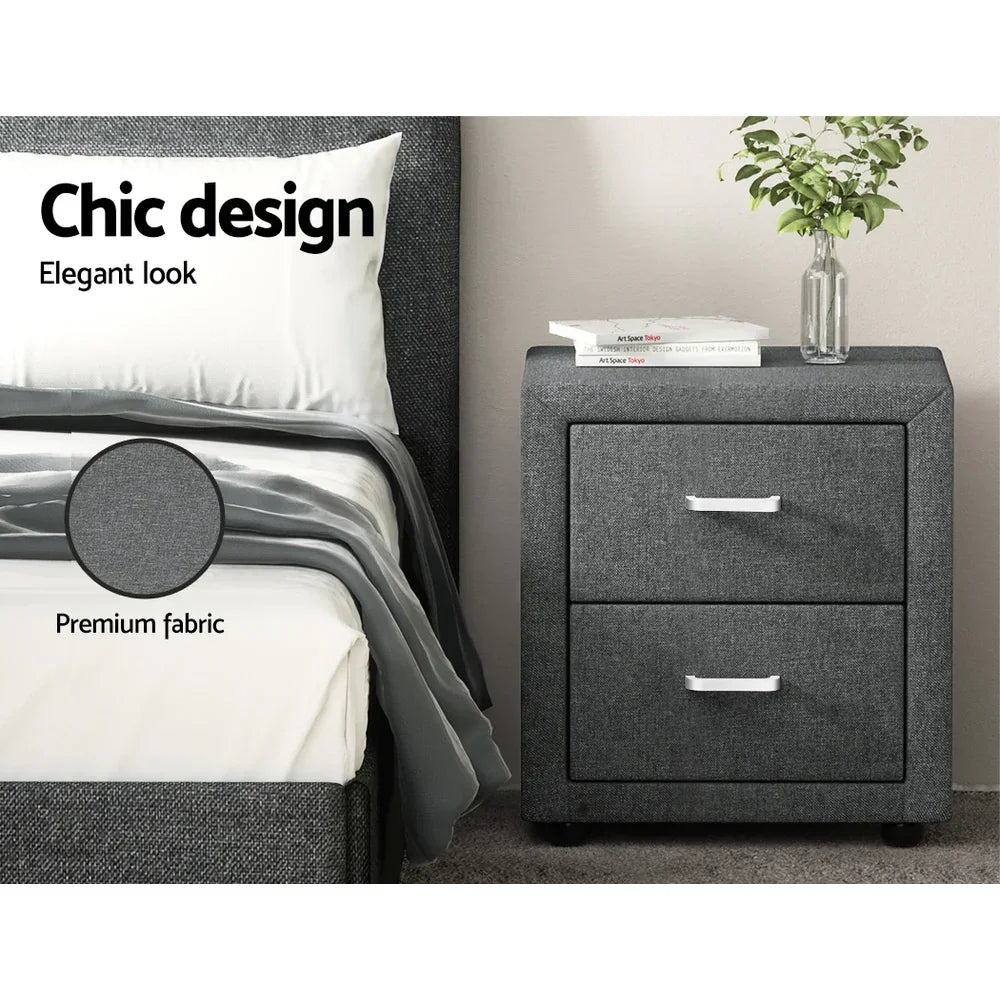 Grey fabric bedside table with two drawers, modern bed, decor books and vase with plant.