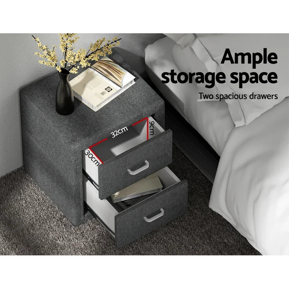 Grey bedside table with two open drawers, vase, books on top, next to a bed, showing drawer dimensions.