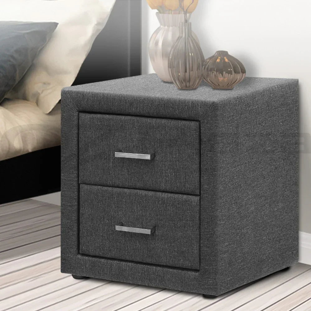 Modern grey bedside table with two drawers and silver handles beside a bed