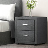 Modern grey fabric bedside table with two drawers, silver handles, and a glass vase