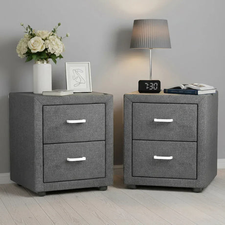 Pair of modern grey fabric bedside tables with drawers, flowers, lamp, books, and clock