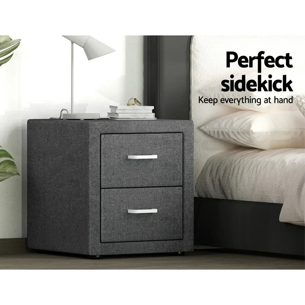 Modern dark grey two-drawer bedside table with lamp and books next to a bed
