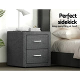 Modern dark grey two-drawer bedside table with lamp and books next to a bed