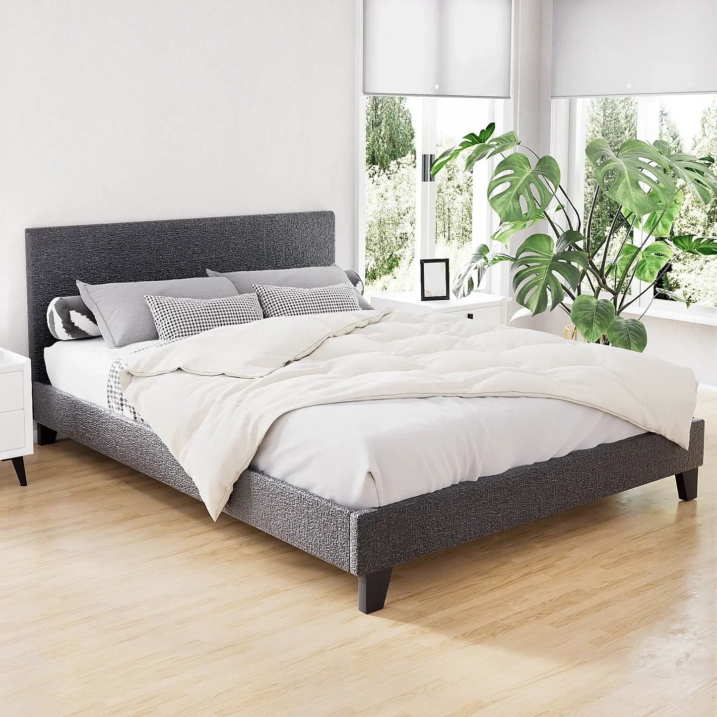 Modern grey fabric bed frame with padded headboard in bright bedroom with large window and plant