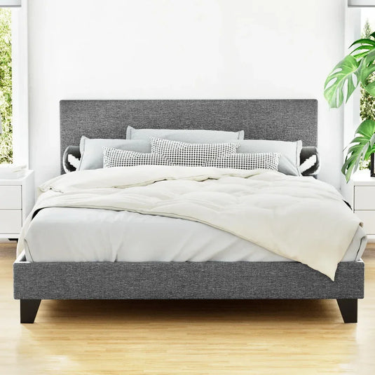 Modern grey upholstered bed frame with headboard, neatly made in a bright bedroom