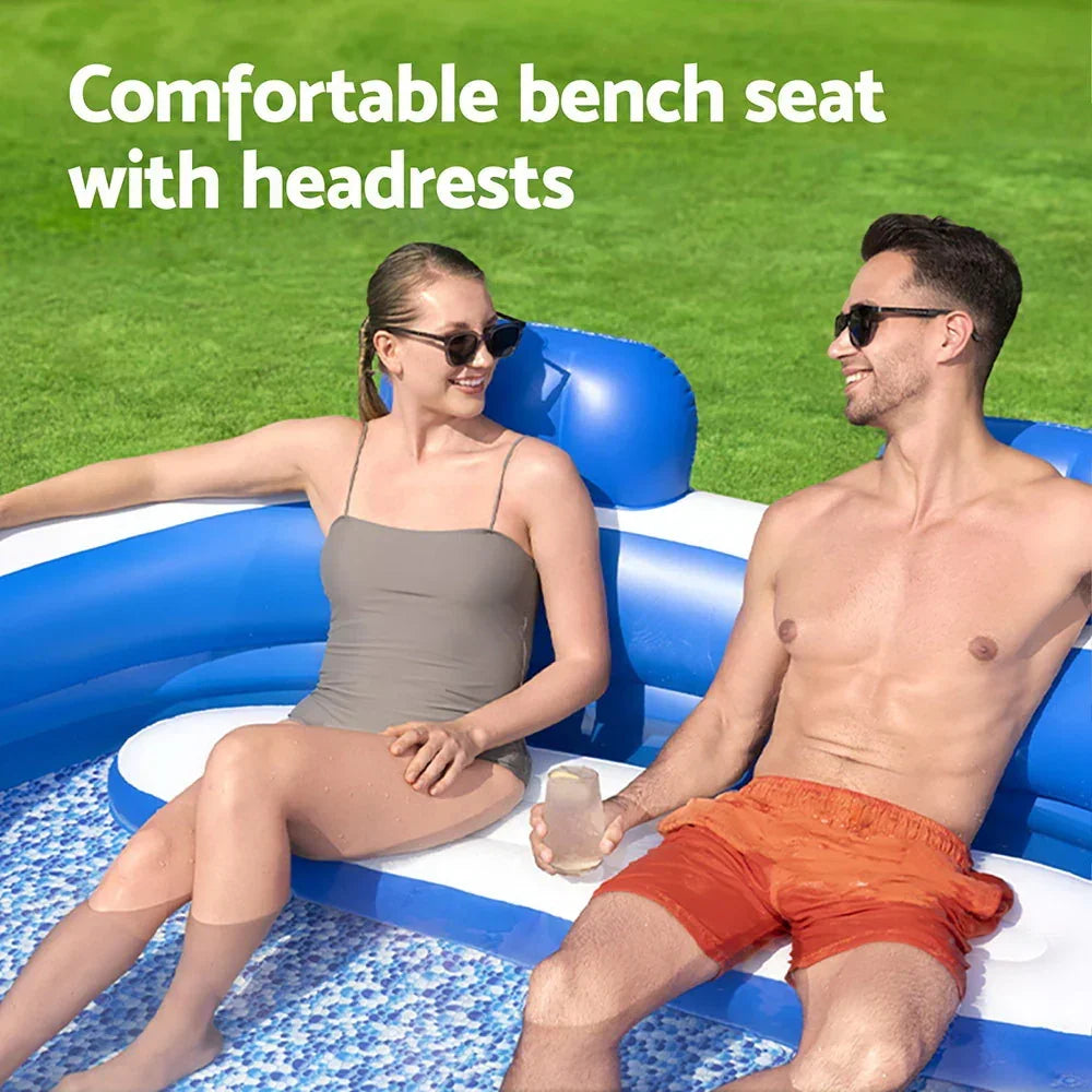 Two people relaxing on an inflatable pool bench seat with headrests, outdoors on grass.