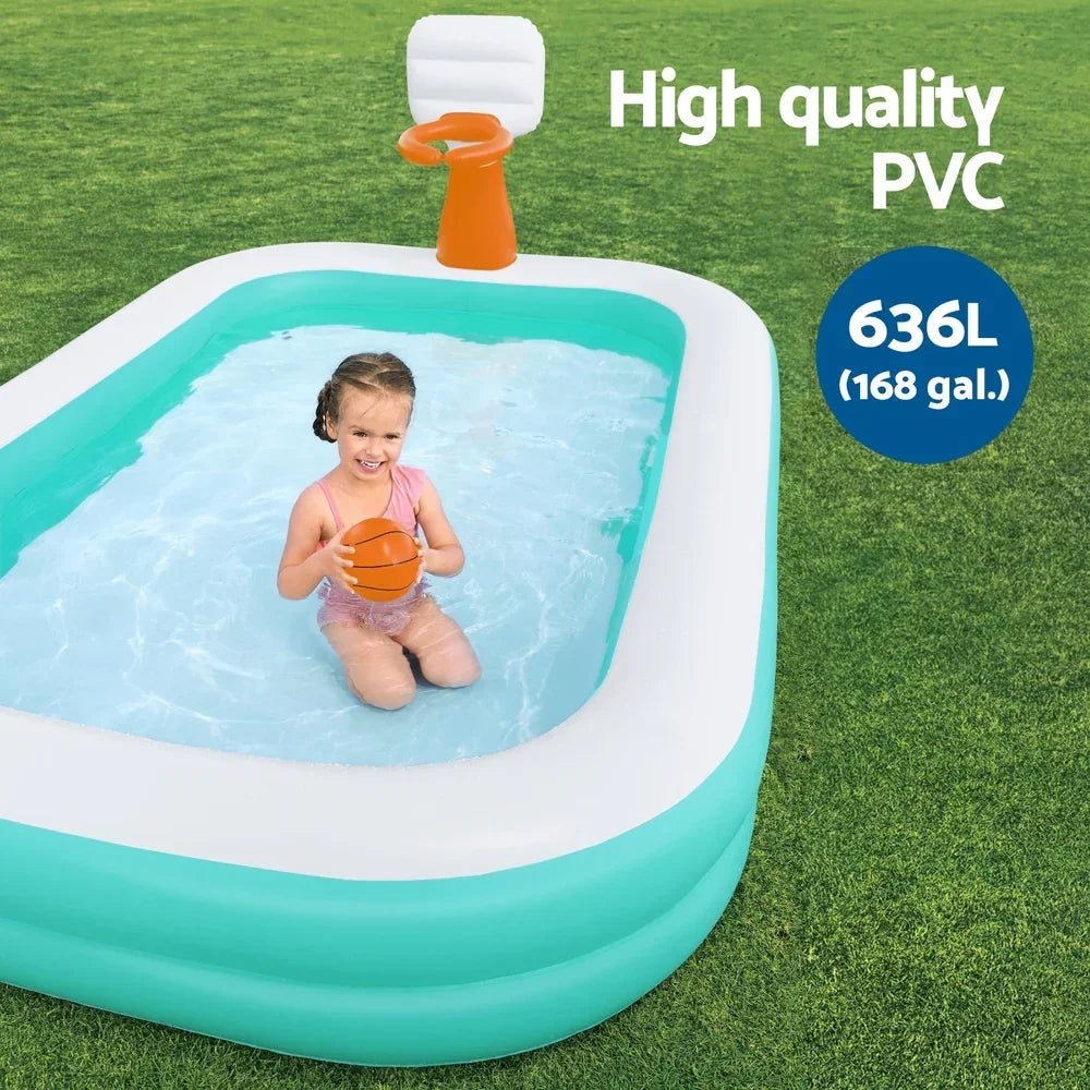 Child playing with ball in inflatable kiddie pool with basketball hoop on green grass outdoors.