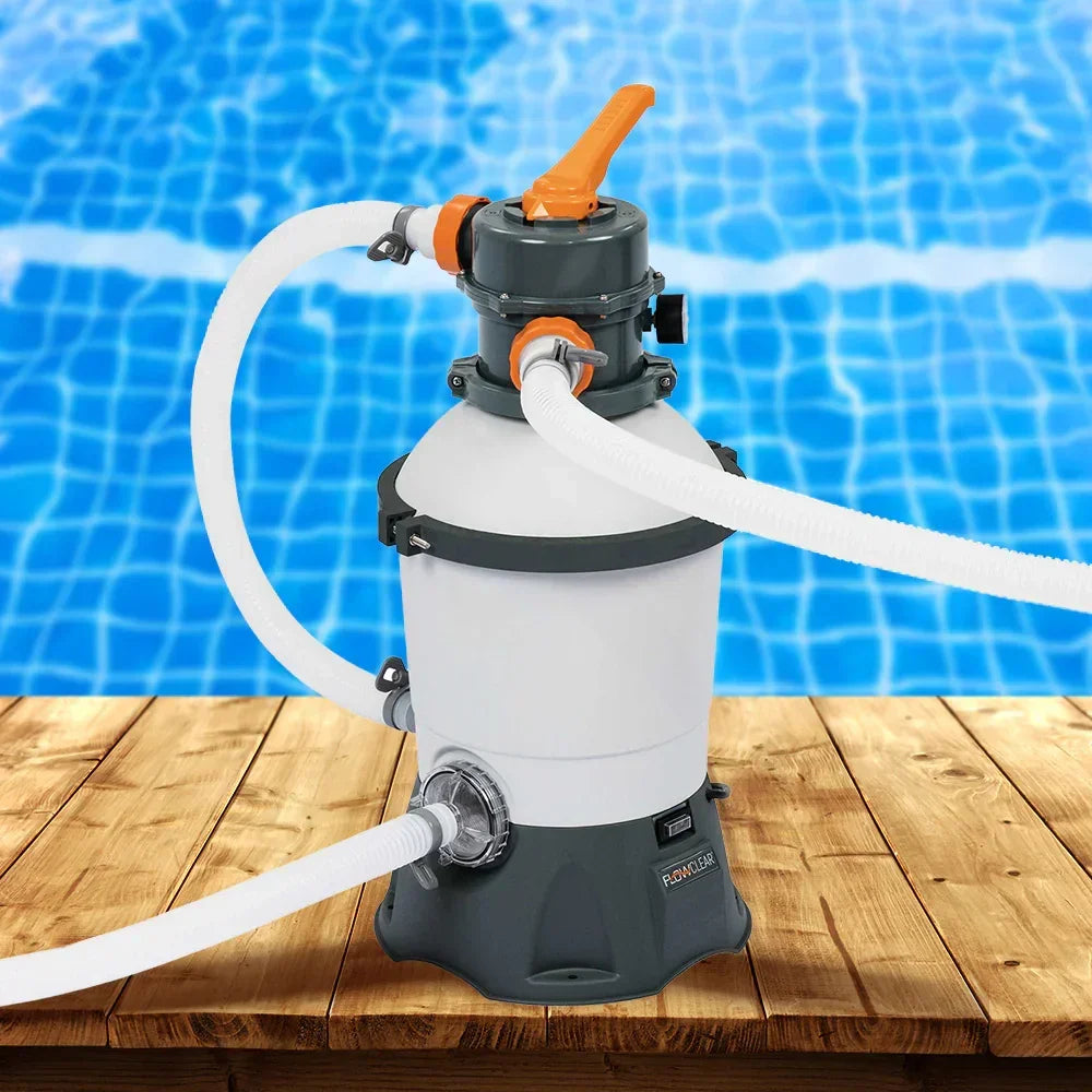 Sand filter pump for swimming pool with hoses on wooden deck by blue pool water