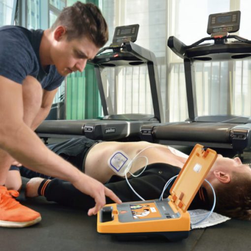 Man using AED defibrillator on person lying near treadmills in gym setting