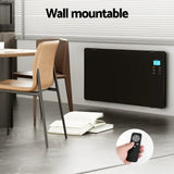 Wall mounted black glass panel heater with digital display and remote control in modern room.
