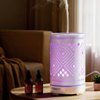 Aromatherapy diffuser with geometric LED lights on a table, steaming, beside essential oil bottles
