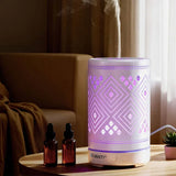 Aromatherapy diffuser with geometric LED lights on a table, steaming, beside essential oil bottles