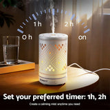 White electric aroma diffuser with geometric cutout patterns, misting on a wooden table indoors.
