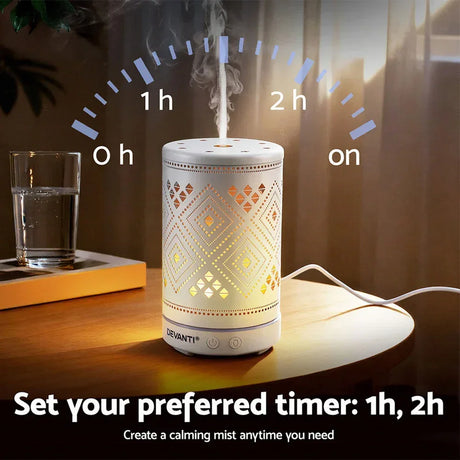 White electric aroma diffuser with geometric cutout patterns, misting on a wooden table indoors.