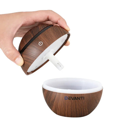 Hand opening a wood grain ultrasonic aroma diffuser with Devanti logo, showing inside compartment.