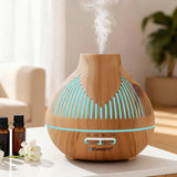 Wood grain essential oil diffuser with LED lights emitting mist, on table with oil bottles