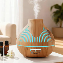 Wood grain essential oil diffuser with LED lights emitting mist, on table with oil bottles