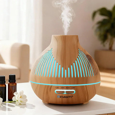Wood grain essential oil diffuser with LED lights emitting mist, on table with oil bottles