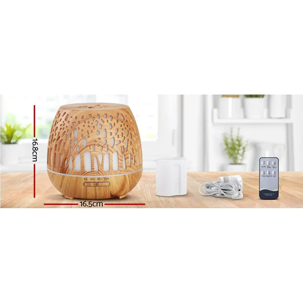 Wood grain essential oil diffuser with remote, measuring cup, and power cord on a kitchen counter.