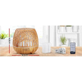 Wood grain essential oil diffuser with remote, measuring cup, and power cord on a kitchen counter.