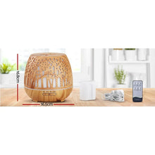 Wood grain essential oil diffuser with remote, measuring cup, and power cord on a kitchen counter.