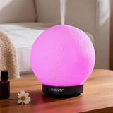 Pink moon-shaped LED aroma diffuser with steam on wooden table in living room setting