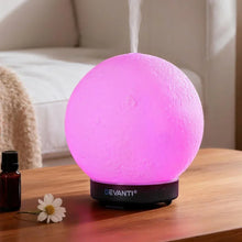 Pink moon-shaped LED aroma diffuser with steam on wooden table in living room setting