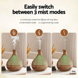 Wood grain essential oil diffuser with three mist modes, emitting vapor on a tabletop indoors.