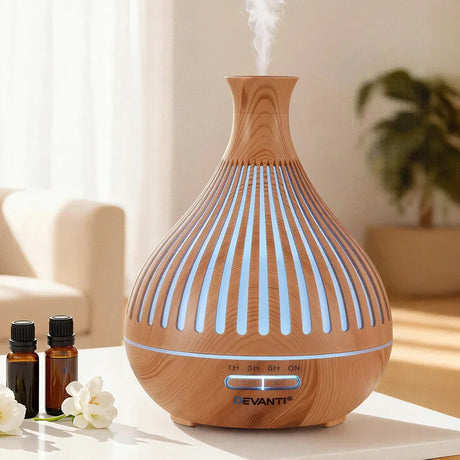 Wood grain essential oil diffuser with LED lights on a table, emitting mist, with oils nearby