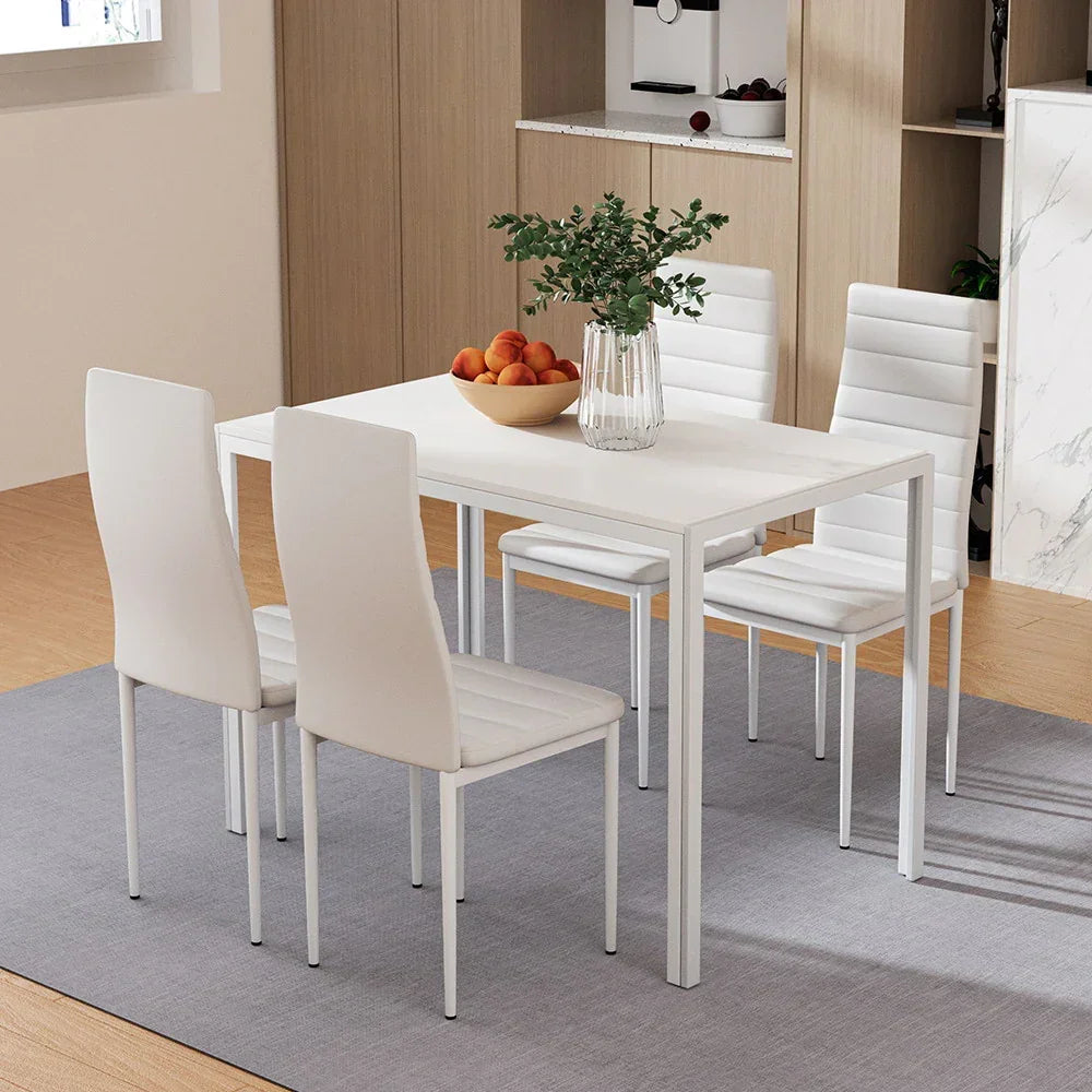 Modern white dining table with four chairs on gray rug, vase and fruit bowl in kitchen setting