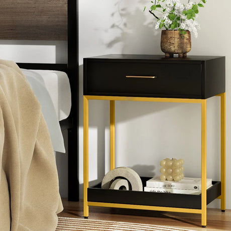 Modern black and gold bedside table with drawer, decorative vase, and decor accents