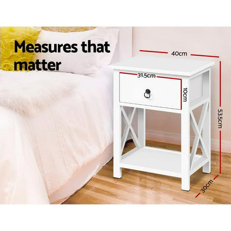 White bedside table with drawer, cross-side design, and measurements shown in bedroom setting.